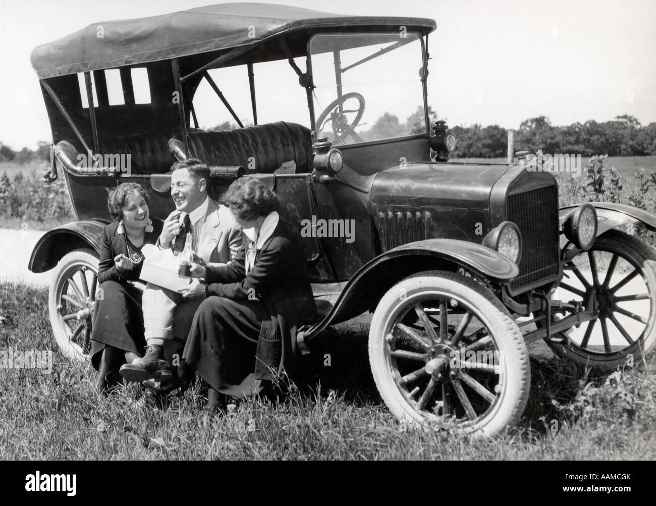 Années 20, DEUX FEMMES ET UN HOMME ASSIS SUR L'EXÉCUTION DU MODÈLE T Ford de manger le déjeuner à parler et rire Banque D'Images