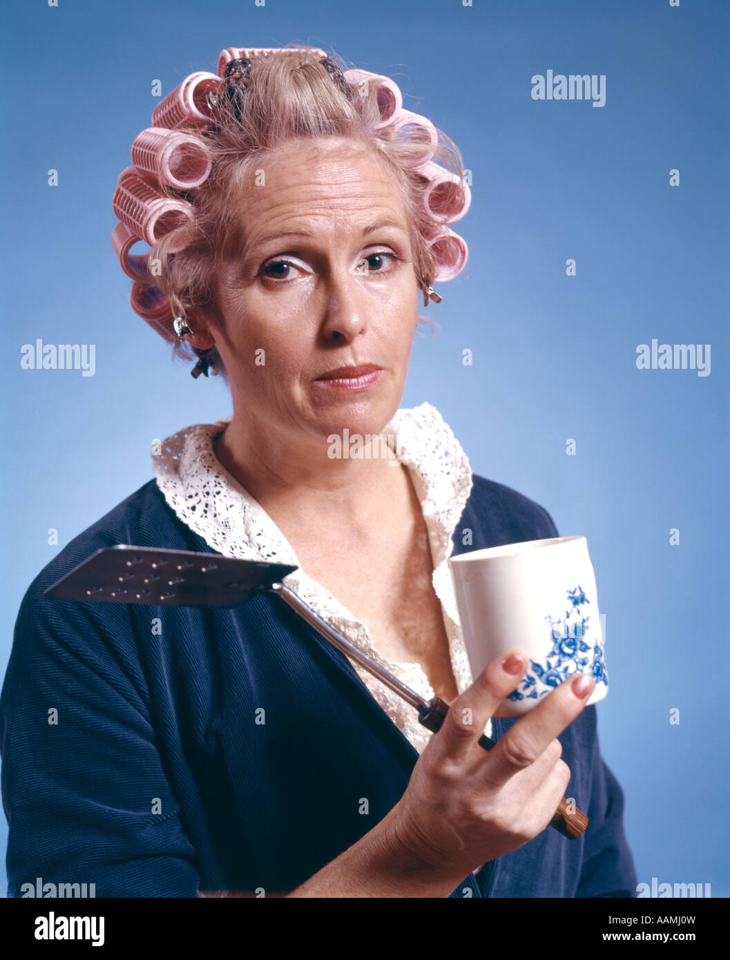 Des années 70, femme d'ÂGE MOYEN PORTANT DES BIGOUDIS ROBE HOLDING EGG  TURNER la spatule COFFEE MUG FEMME AU FOYER LE PETIT DÉJEUNER DU MATIN  Photo Stock - Alamy