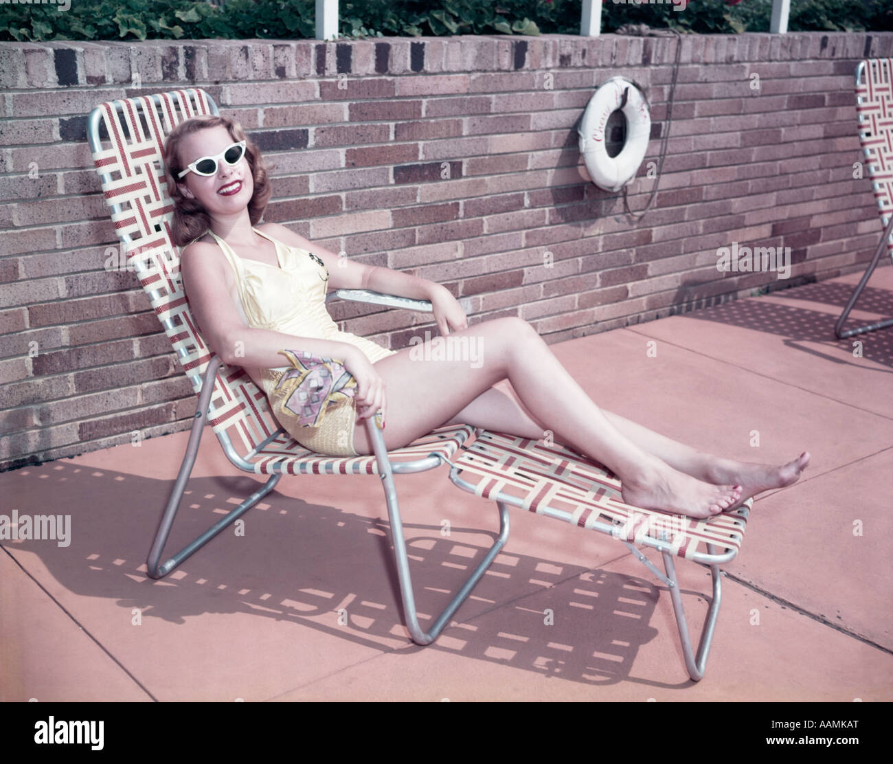 1950 FEMME portant des lunettes de soleil dans une chaise longue chaise longue LIFE PRESERVER BOUÉE SUR MUR DE PIERRE Banque D'Images