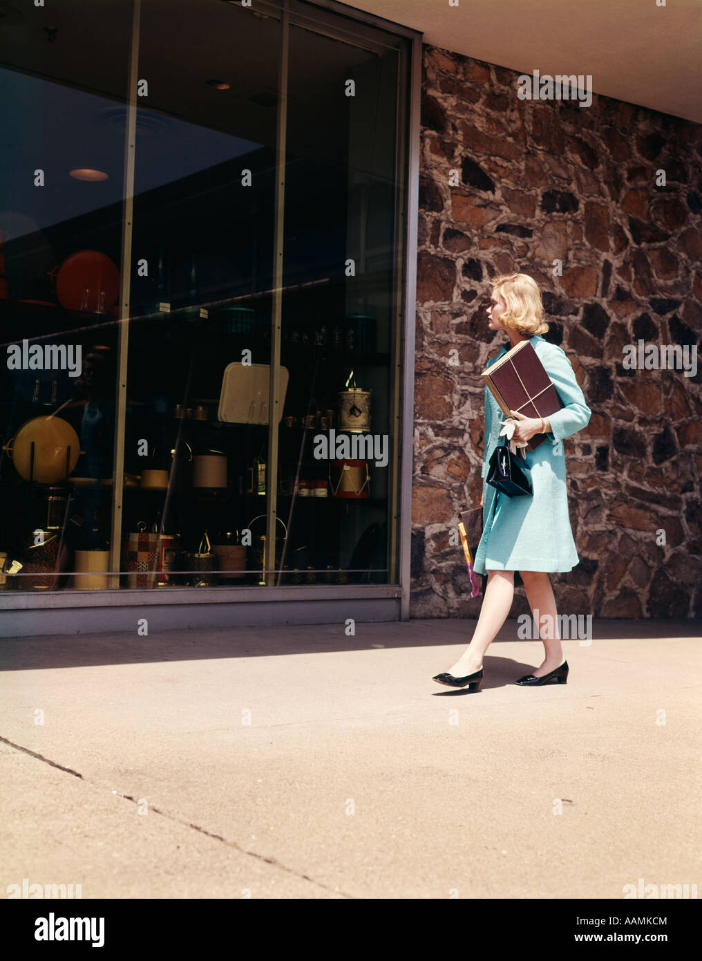1960 1960 Femme blonde BLUE COAT WALKING DOWN STREET WINDOW SHOPPING À LA BOUTIQUE DE VENTE AU DÉTAIL EN MAGASIN WINDOWS RETRO Banque D'Images
