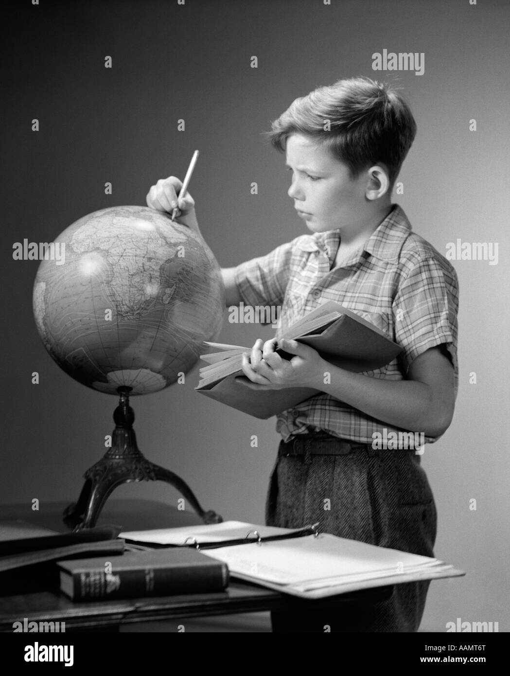 Années 1940 Années 1950 SERIOUS BOY RECHERCHE DE LIEU SUR TERRE GLOBE AVEC CRAYON TENIR GÉOGRAPHIE LIVRE OUVERT Banque D'Images