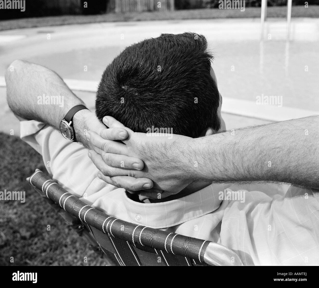 1970 Close-up VUE ARRIÈRE DE L'HOMME AVEC LES mains croisées derrière la tête allongé dans une chaise longue piscine Banque D'Images