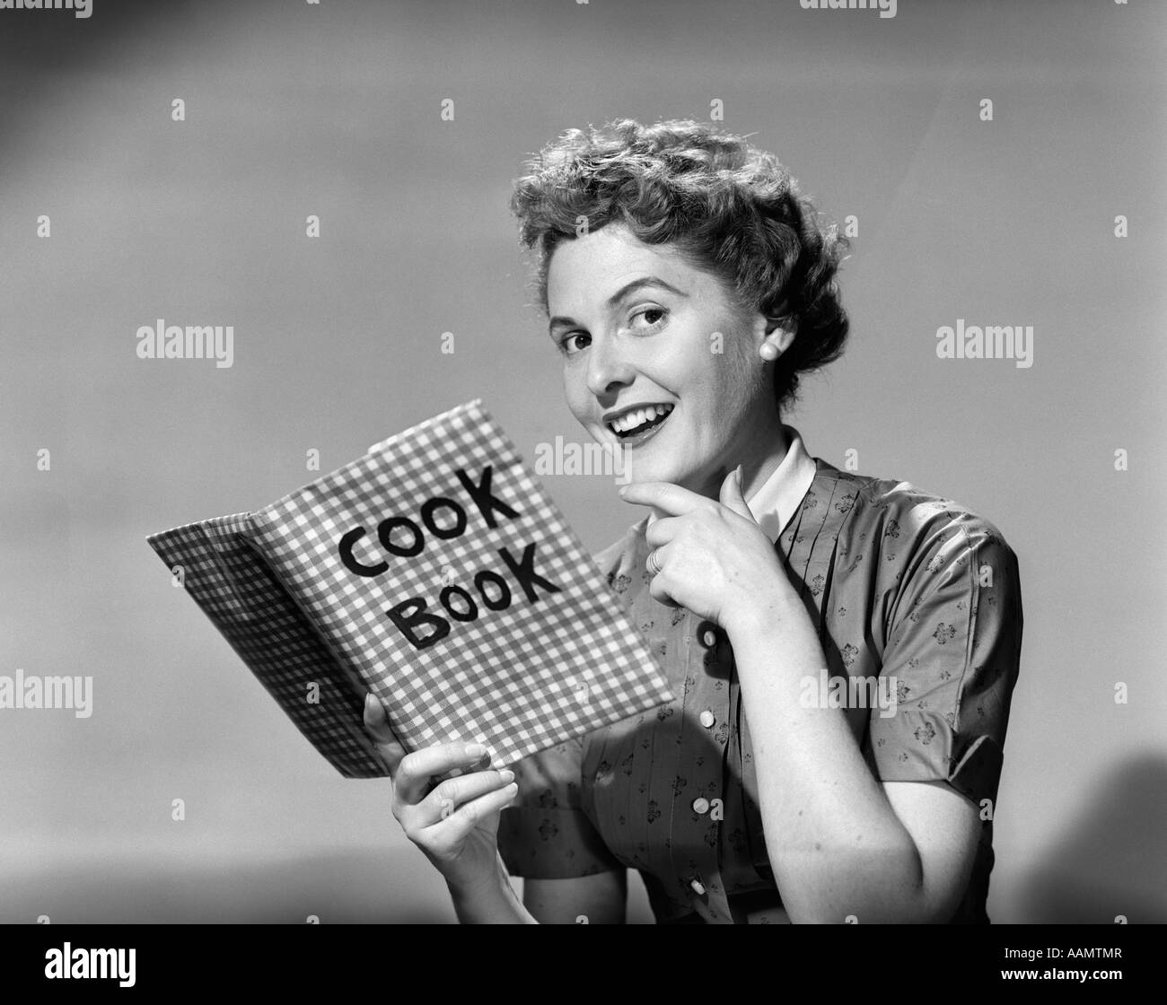 1950 SMILING WOMAN HOLDING COOKBOOK LOOKING AT CAMERA Banque D'Images