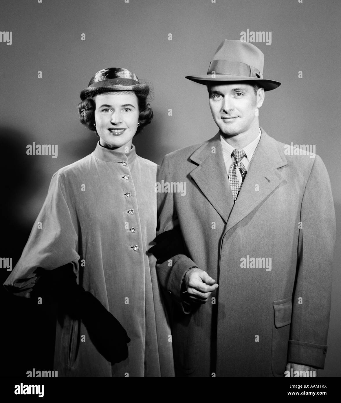 Années 1940 Années 1950 COUPLE HOMME FEMME côte à côte, PORTANT LES VÊTEMENTS D'EXTÉRIEUR manteaux et chapeaux LOOKING AT CAMERA Banque D'Images