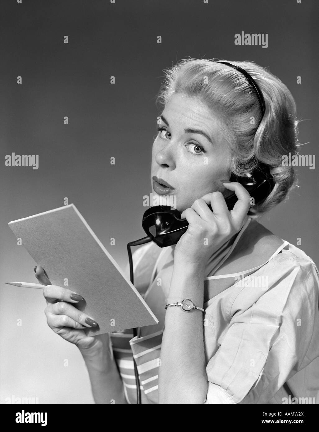 Années 1950 Années 1960 BLONDE WOMAN HOLDING TÉLÉPHONE CRAYON & TABLET LOOKING AT CAMERA Banque D'Images