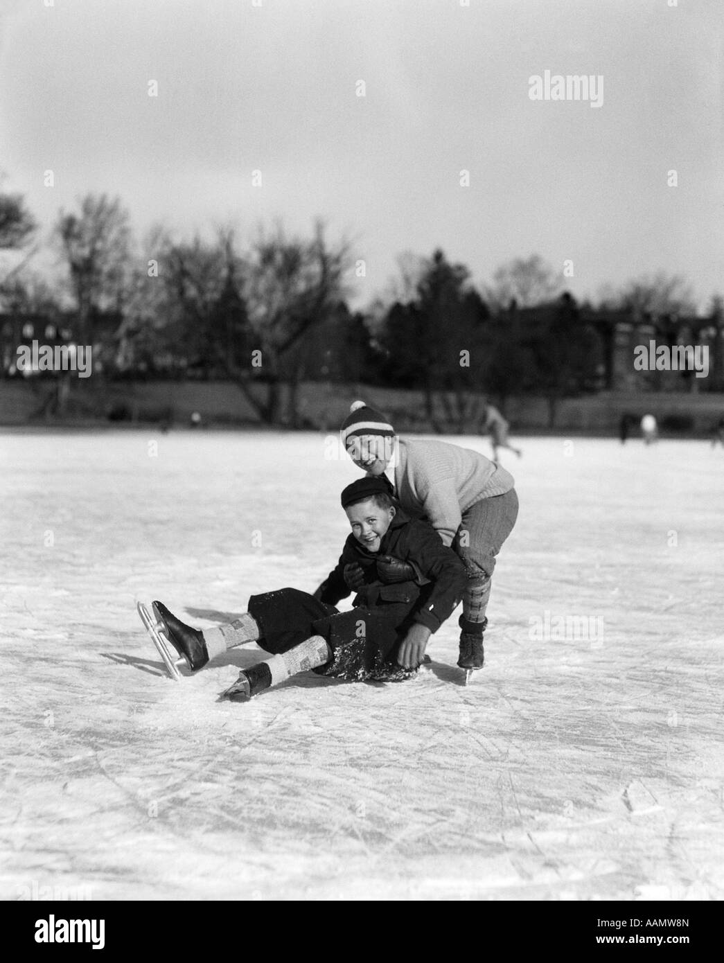 Années 1920 Années 1930 DEUX GARÇONS SMILING AT CAMERA patin à glace UN GARÇON tombé d'autres LUI CUEILLETTE Banque D'Images
