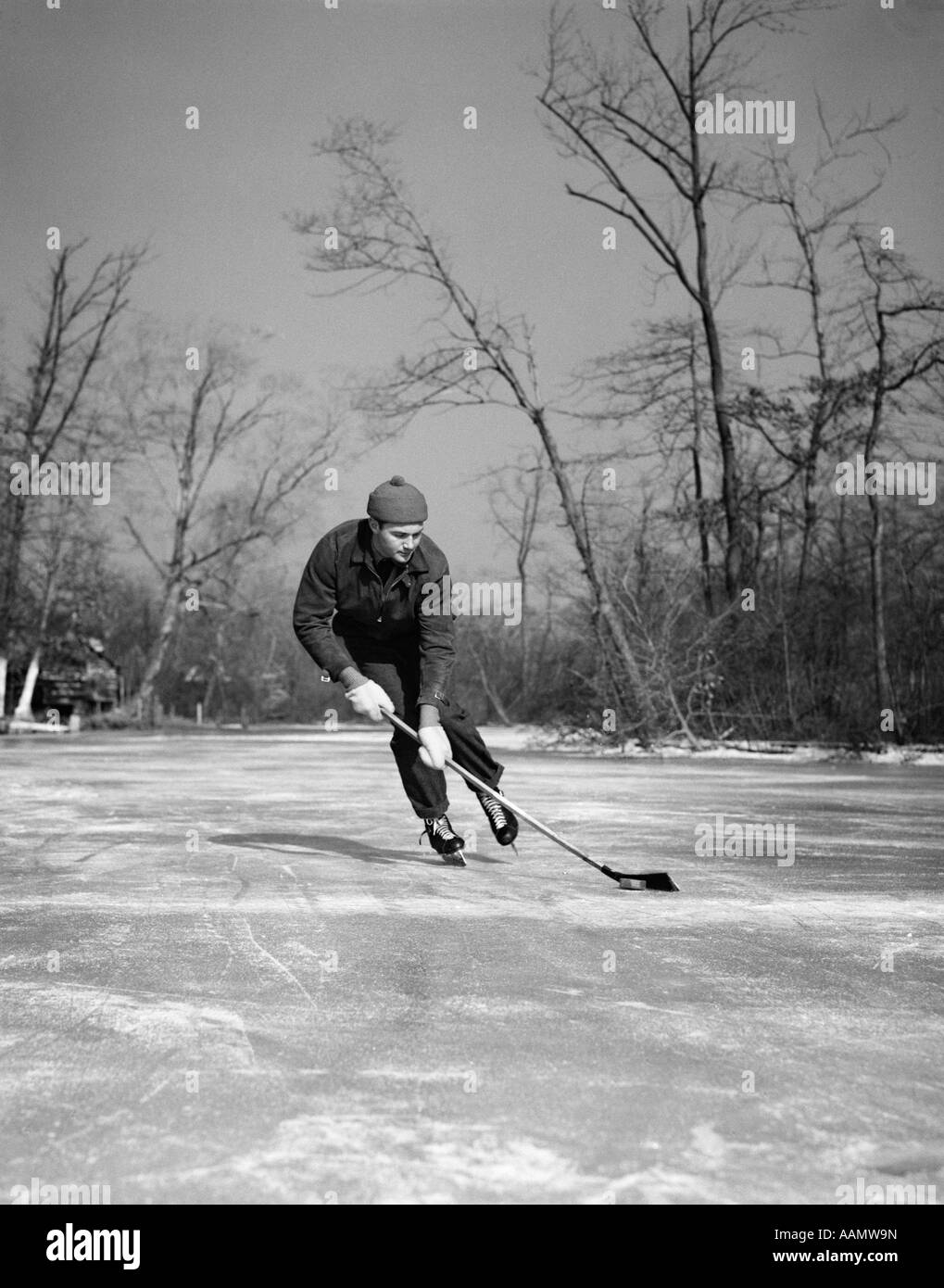 1940 MAN PLAYING ICE HOCKEY SUR LAC GELÉ LE CONTRÔLE DE RONDELLE AVEC STICK Banque D'Images