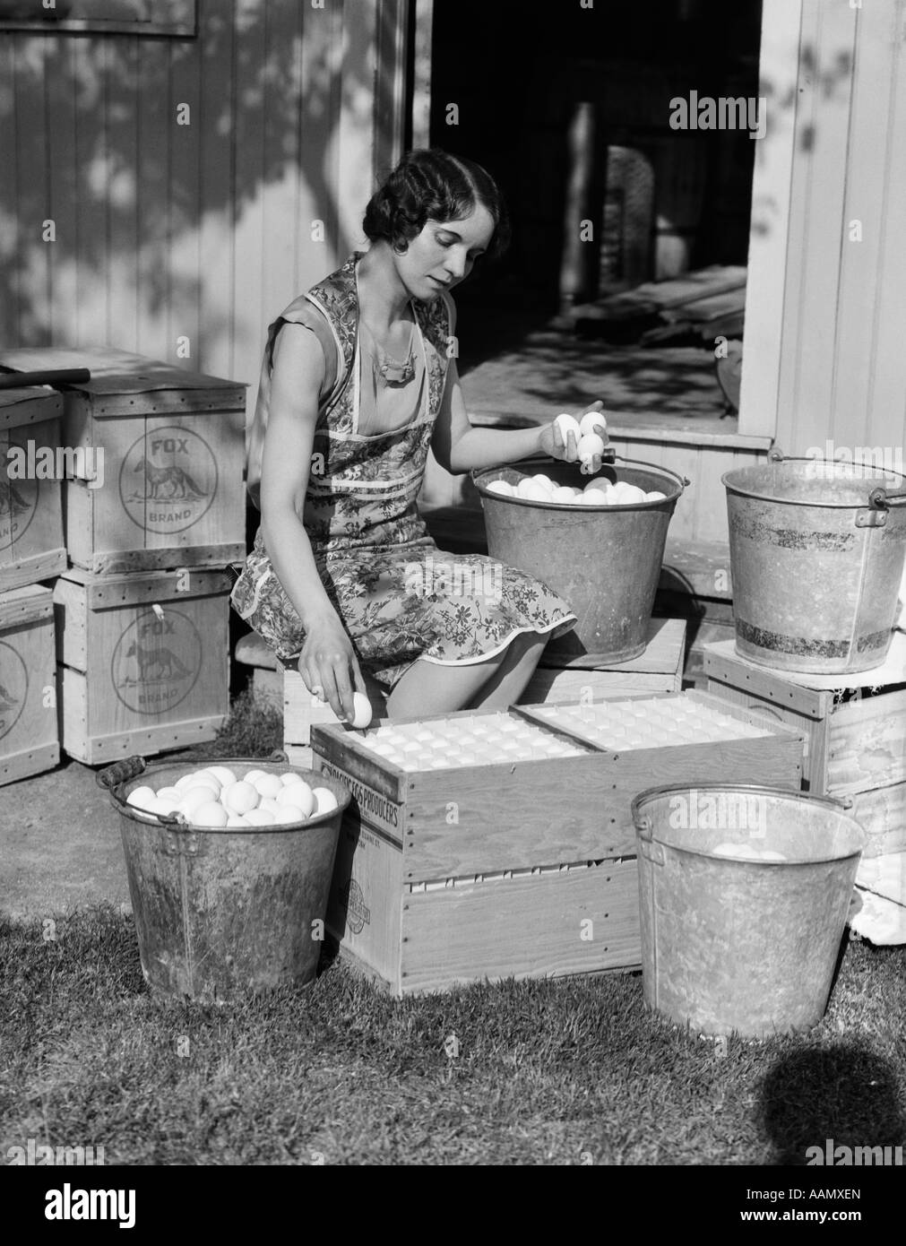 1930 Ferme femme femme assis à l'extérieur du poulailler PORTE OEUFS METTRE DANS DES SEAUX DE CAISSES DE TRANSPORT Banque D'Images