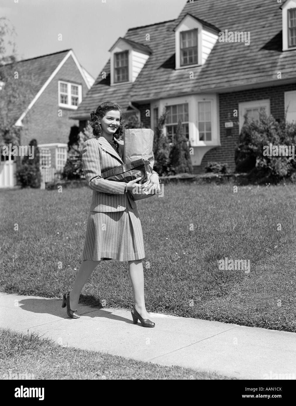 1940 WOMAN WALKING SHOPPING SAC DE TRANSPORT SUR TROTTOIR MAISON DE BANLIEUE Banque D'Images