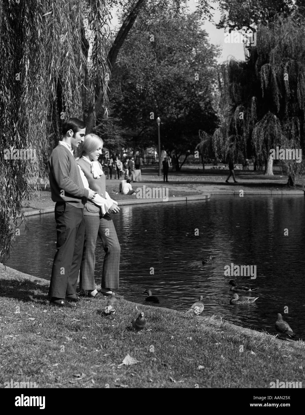 1960 COUPLE MAN & Woman feeding DUCKS SUR PARC étang entouré d'ARBRES Banque D'Images