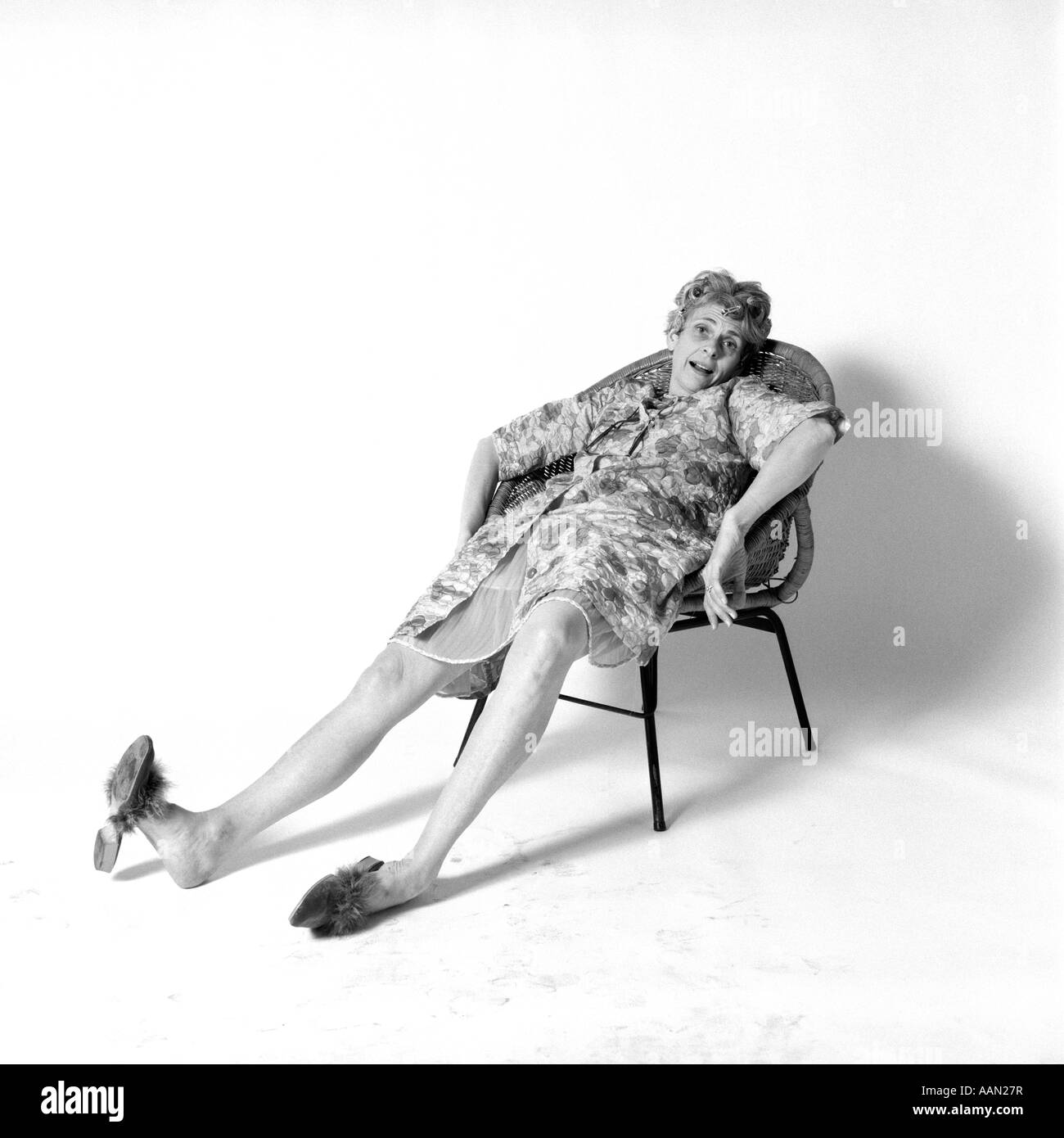 1970 FEMME SLOUCHED DANS CHAISE AVEC EXPRESSION portant robe de robe de nuit épuisé chaussons Banque D'Images