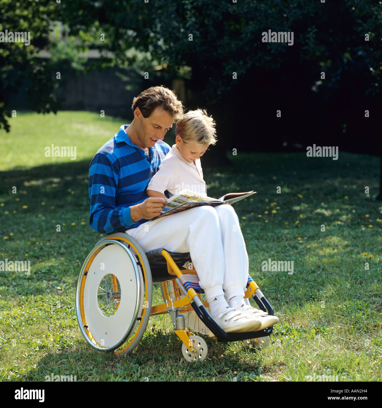 Homme handicapé en fauteuil roulant lisant un livre à un petit garçon dans le jardin Banque D'Images