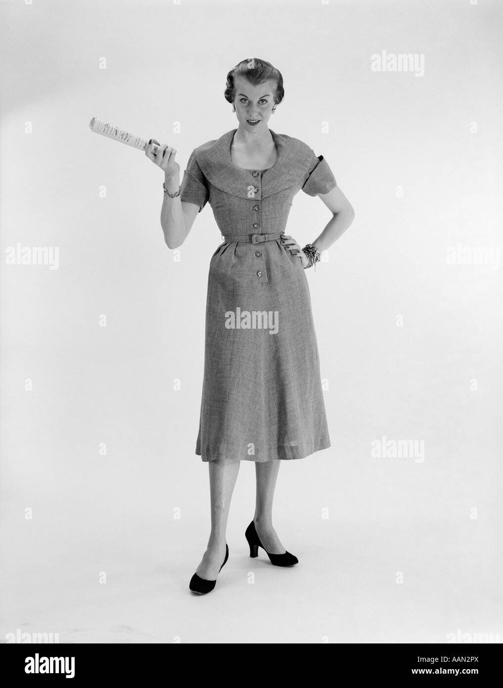 1950 WOMAN STANDING WITH HAND ON HIP HOLDING PAPER LOOKING AT CAMERA Banque D'Images