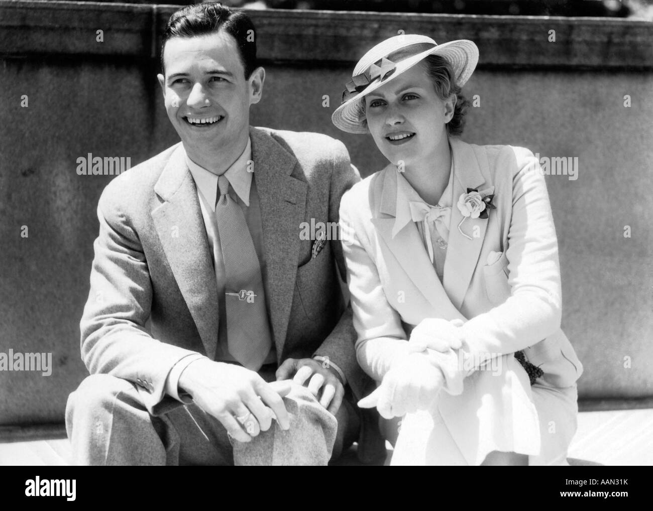1930 SMILING COUPLE ASSIS À L'EXTÉRIEUR DANS LA LUMIÈRE DU SOLEIL Banque D'Images