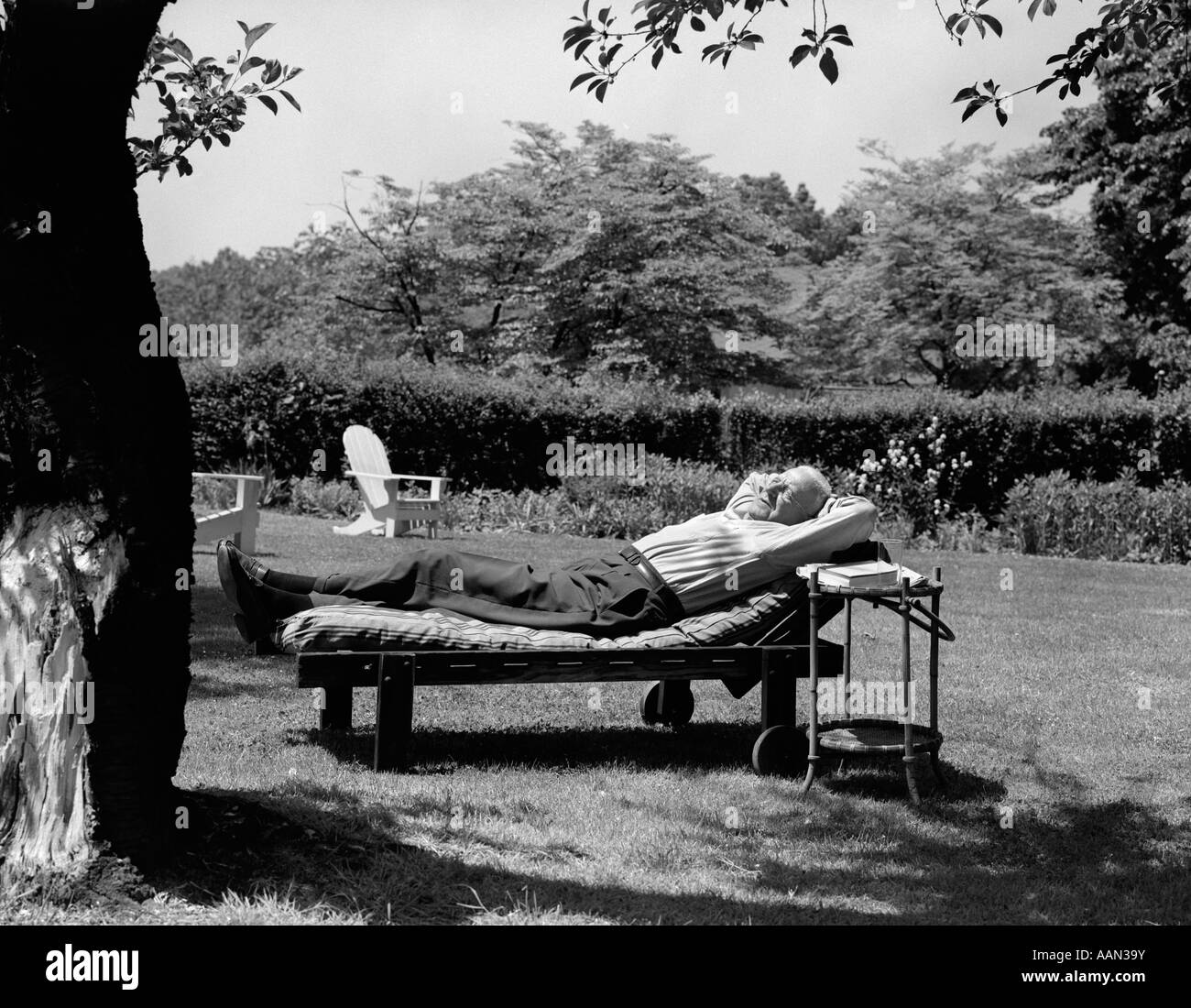 Années 1950, un homme âgé dans jardin allongé sur une chaise longue en vertu de l'arbre Banque D'Images