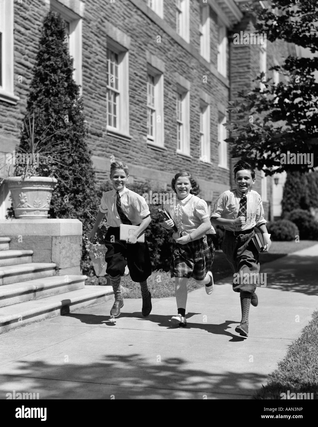 1940 GROUPE DE TROIS ENFANTS DE L'ÉCOLE 2 Garçons 1 fille sur trottoir portant des livres Banque D'Images