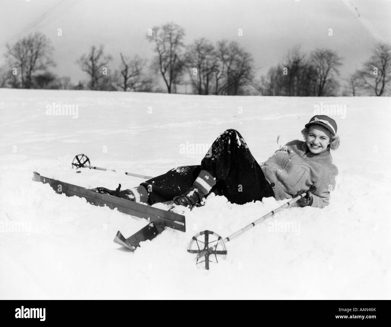 Années 1940 Années 1950 SMILING WOMAN LOOKING AT CAMERA TOMBÉ couché dans la neige avec des skis en bois et les poteaux de bambou Banque D'Images