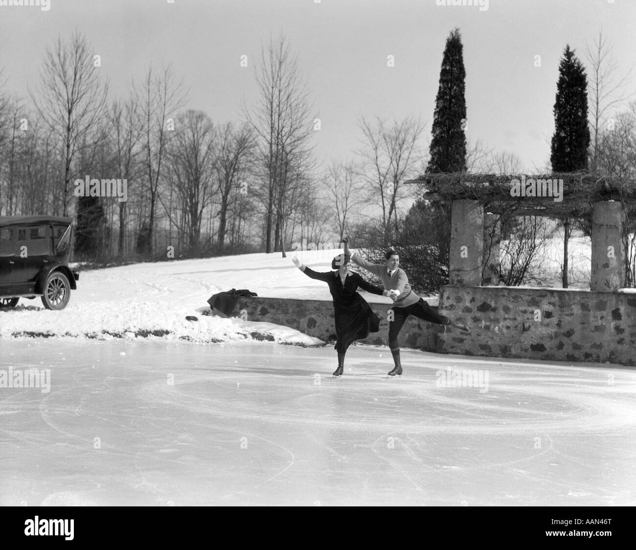 Années 1920 COUPLE HOMME FEMME patin à glace sur une patinoire extérieure À PROXIMITÉ DE VOITURE AVEC ROUES ALIGNÉES côte à côte Banque D'Images
