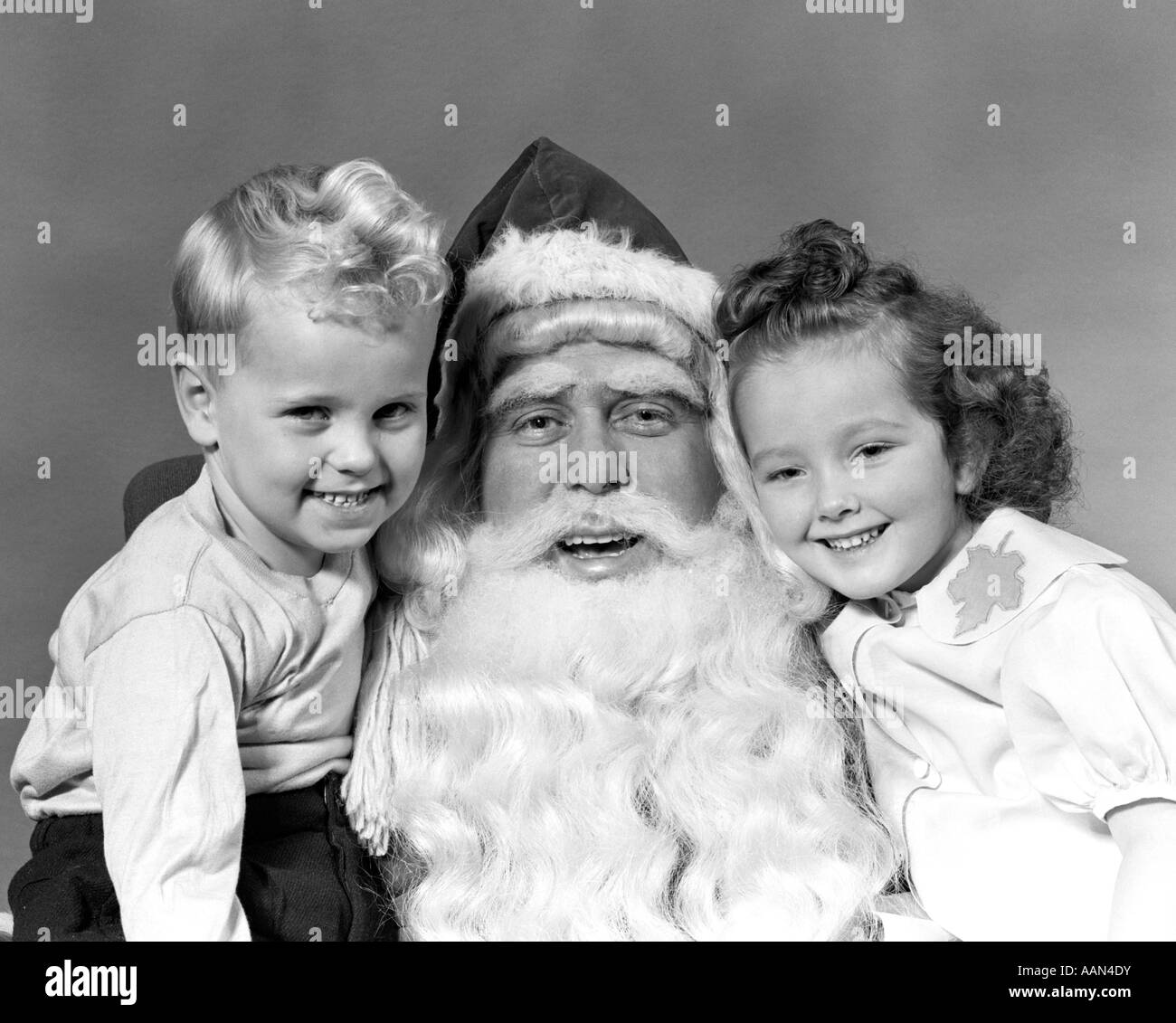 1940 PÈRE NOËL homme posant avec un jeune garçon et d'une jeune fille à genoux SMILING TOUS LOOKING AT CAMERA Banque D'Images