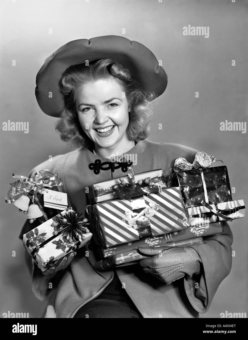 1940 WOMAN IN HAT HOLDING GIFTS SMILING AT CAMERA Banque D'Images