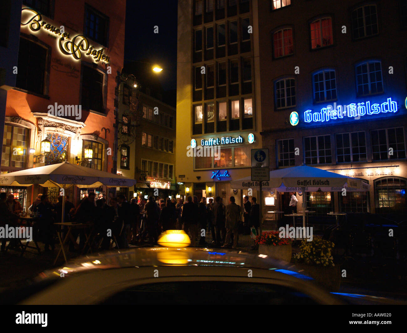 Vie nocturne animée dans les rues de Cologne avec un taxi passant l'allemand typique biergartens Cologne Allemagne Banque D'Images