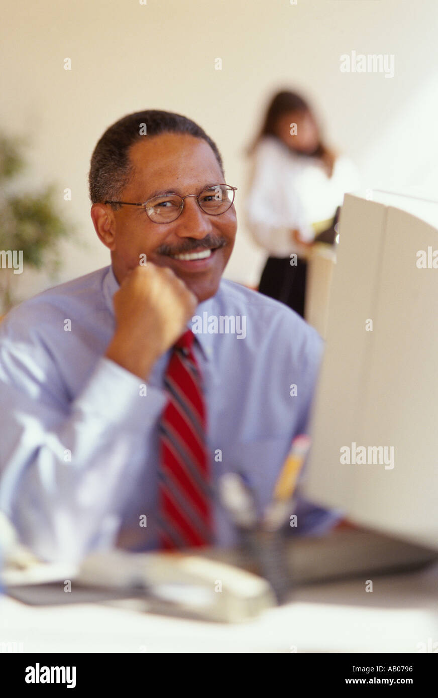 African American Male assis à son bureau exécutif et souriant Banque D'Images