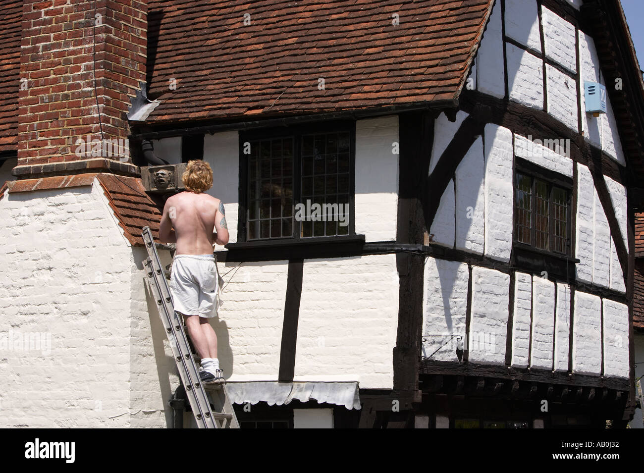 Workman avec échelle sur l'extérieur d'un vieux tudor cottage en été à Shere Surrey England UK Banque D'Images
