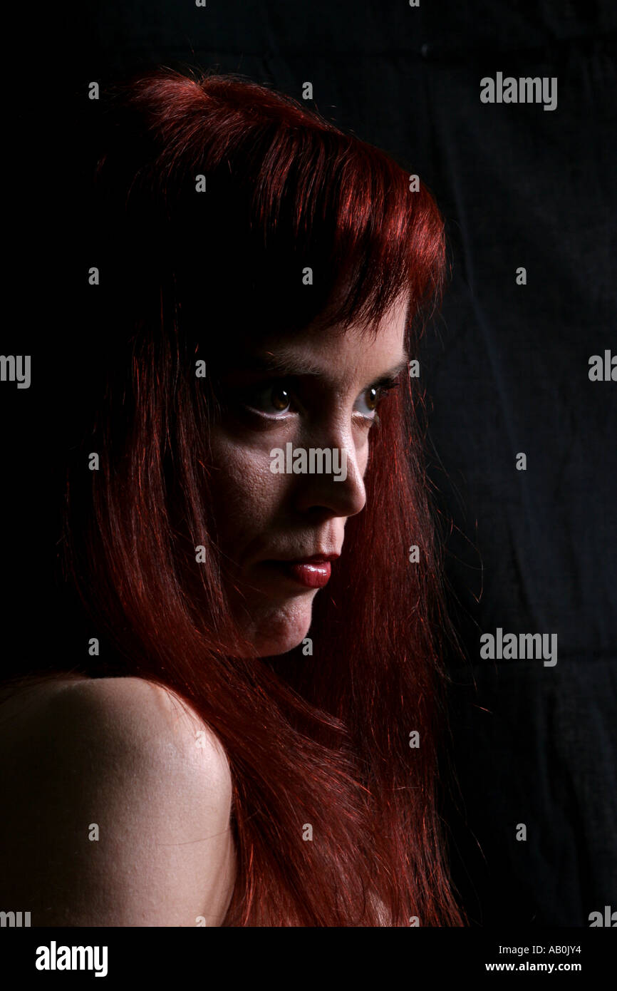 Red Headed Woman en 30s avec visage tourné de trois quarts vers l'afficheur et l'éclairage de la touche basse forte en haut. Banque D'Images