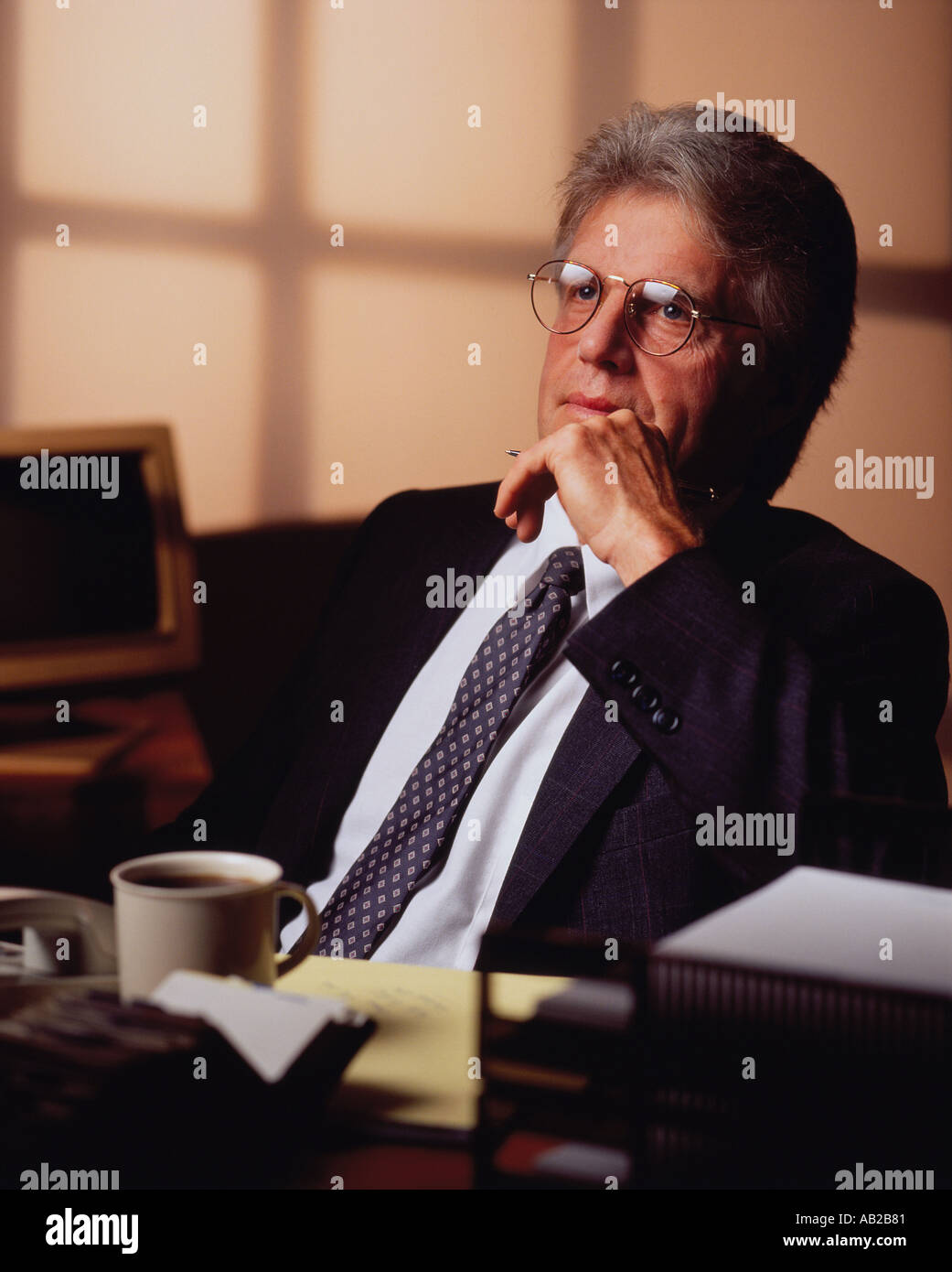 L'homme d'affaires de race blanche d'âge moyen portant des lunettes en se penchant en arrière sur sa chaise avec sa pensée sur son bureau tasse à café Banque D'Images