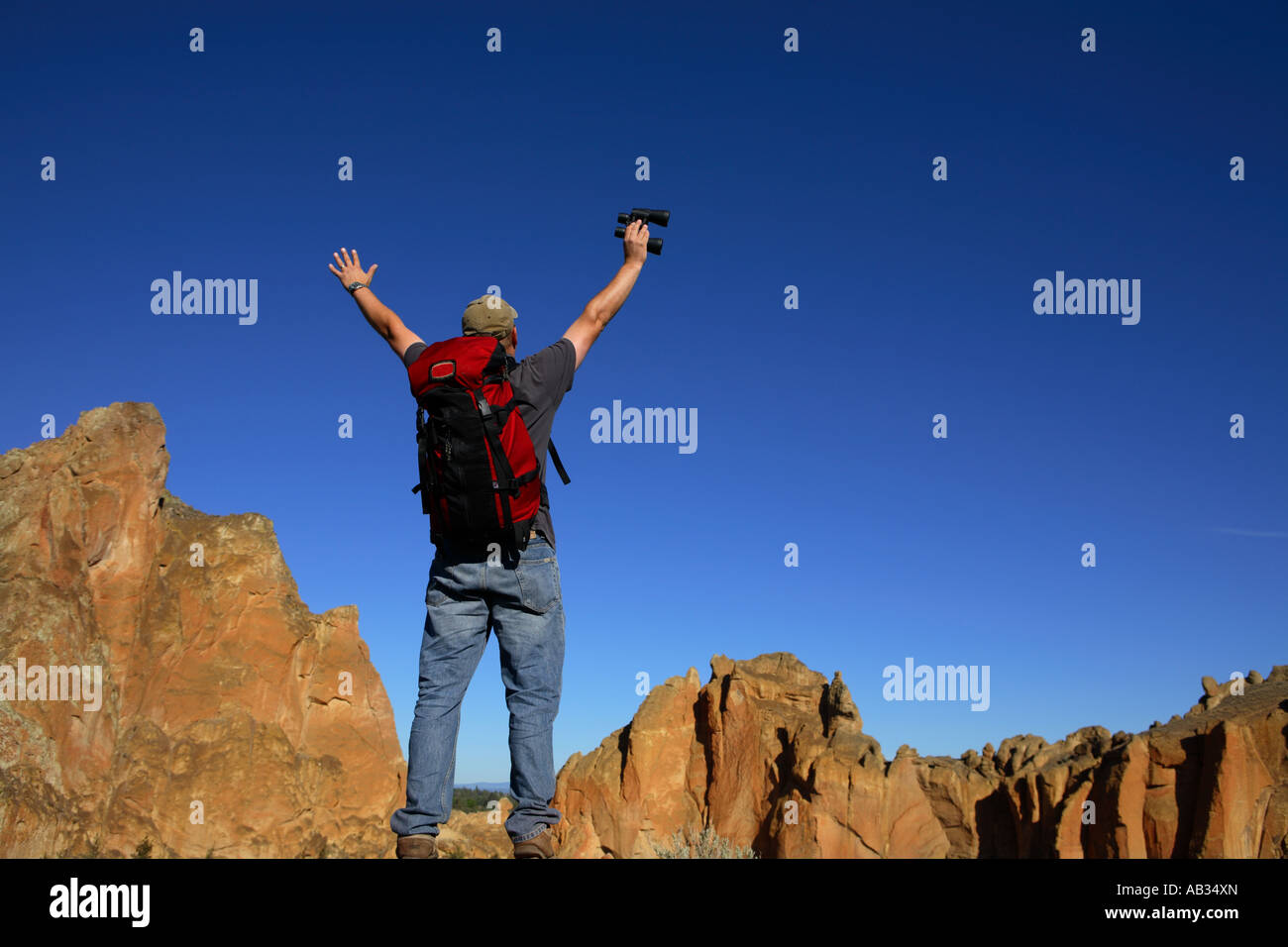 Homme portant un sac à dos se tient avec les mains dans l'air dans un paysage rocheux Banque D'Images
