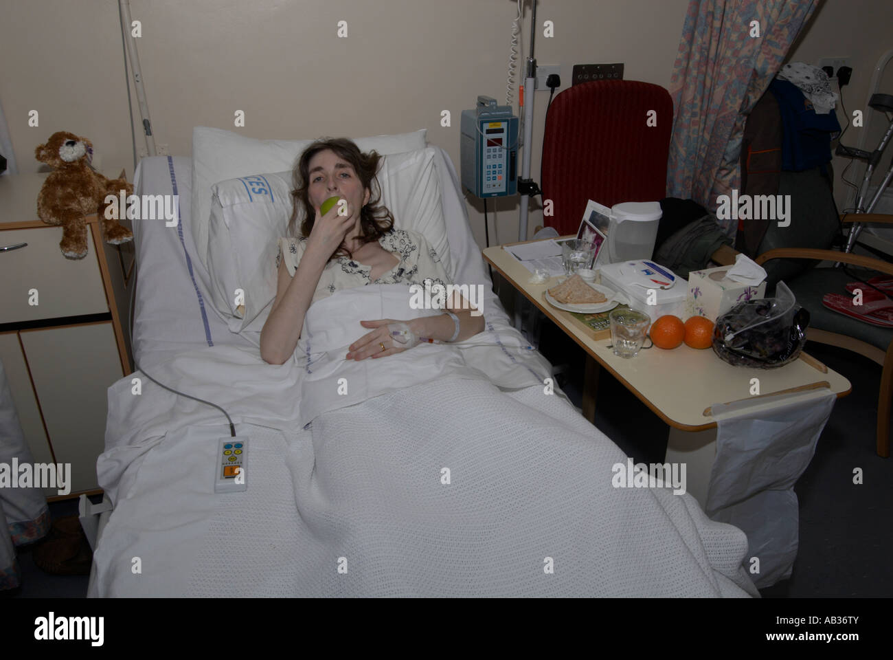 Female patient in cancer ward mangeant une pomme saine surveillées par son compagnon en peluche dans son 30s / 40s Banque D'Images