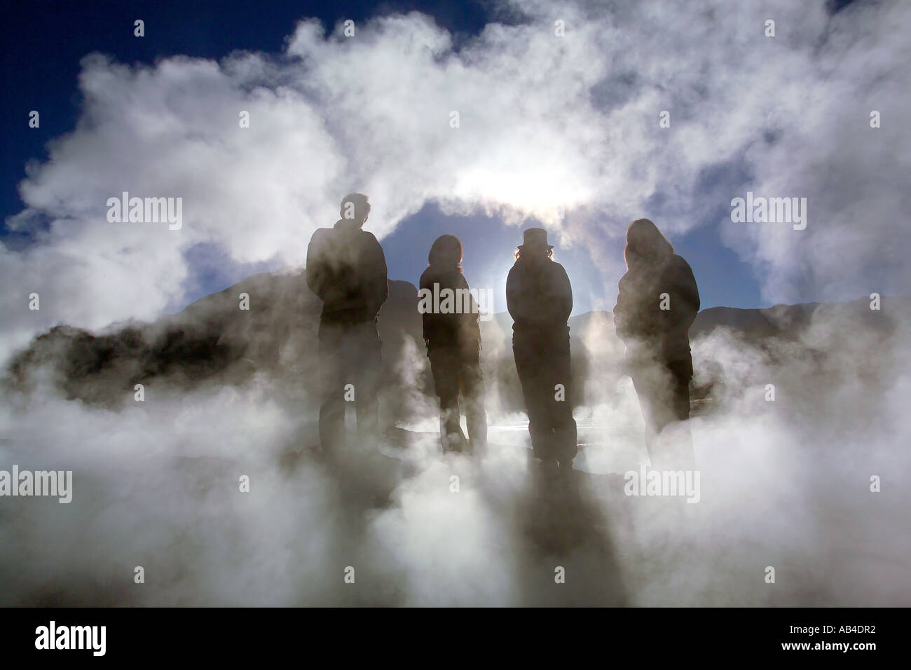 Quatre touristes qui se profile entre la vapeur de la geysers de El Tatio dans le soleil matinal. Banque D'Images