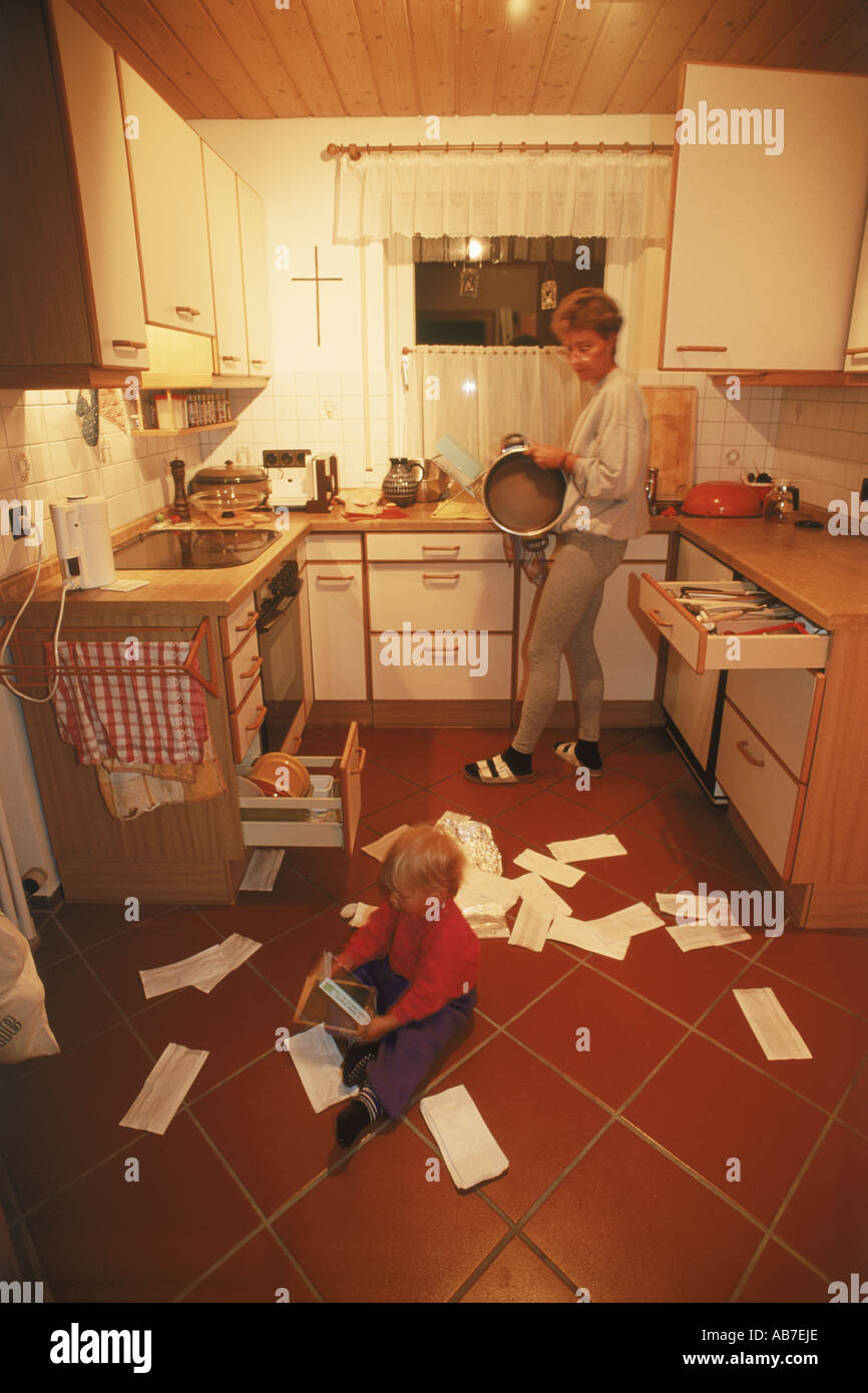 Faire des travaux ménagers Mère avec enfant faisant désordre sur plancher de la cuisine Banque D'Images