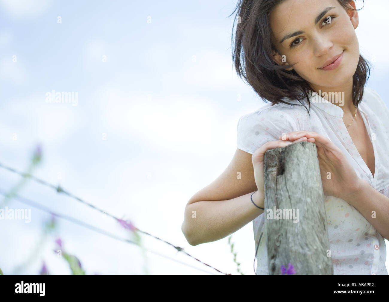 Woman leaning on fence post, looking at camera Banque D'Images