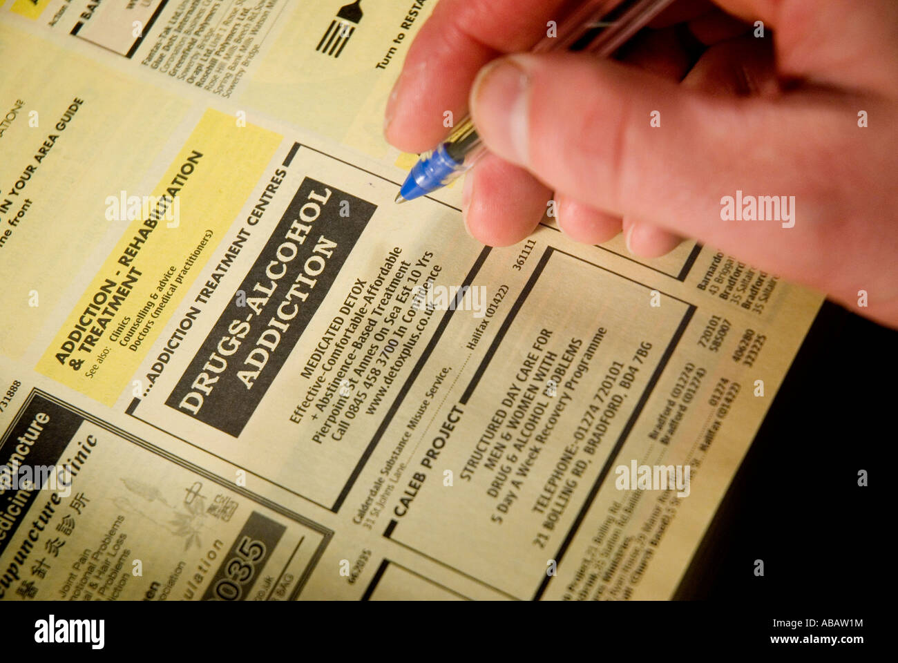 Close up of a mans main avec un annuaire téléphonique des pages jaunes le livre est ouvert à la page énumérant les demandes d'indemnisation entreprises Banque D'Images