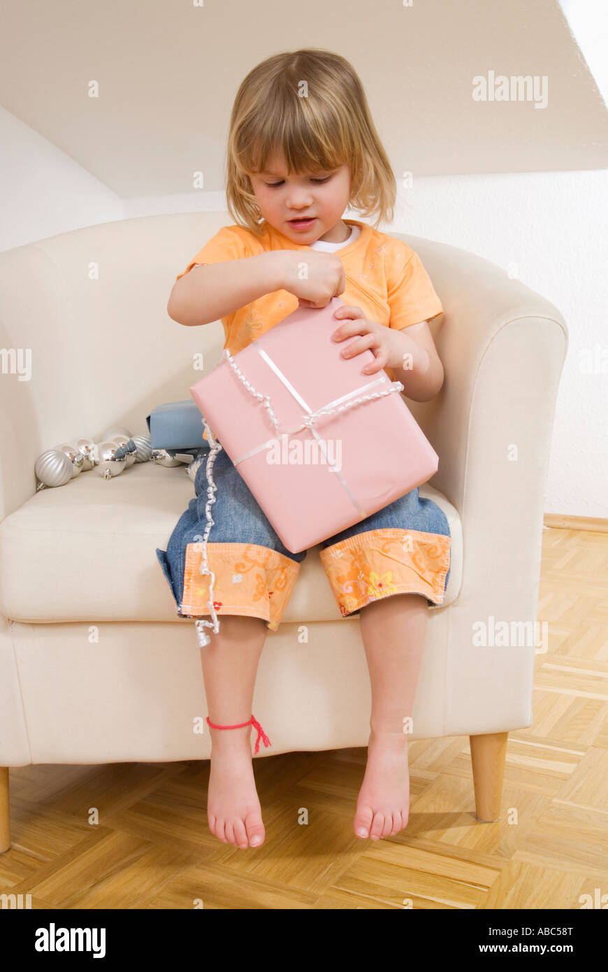 Little girl sitting on chair unwrapping christmas present Banque D'Images