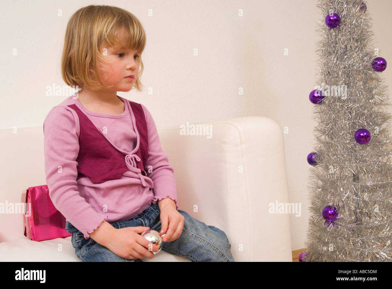 Petite fille assise sur le canapé près de l'arbre de Noël à la triste Banque D'Images