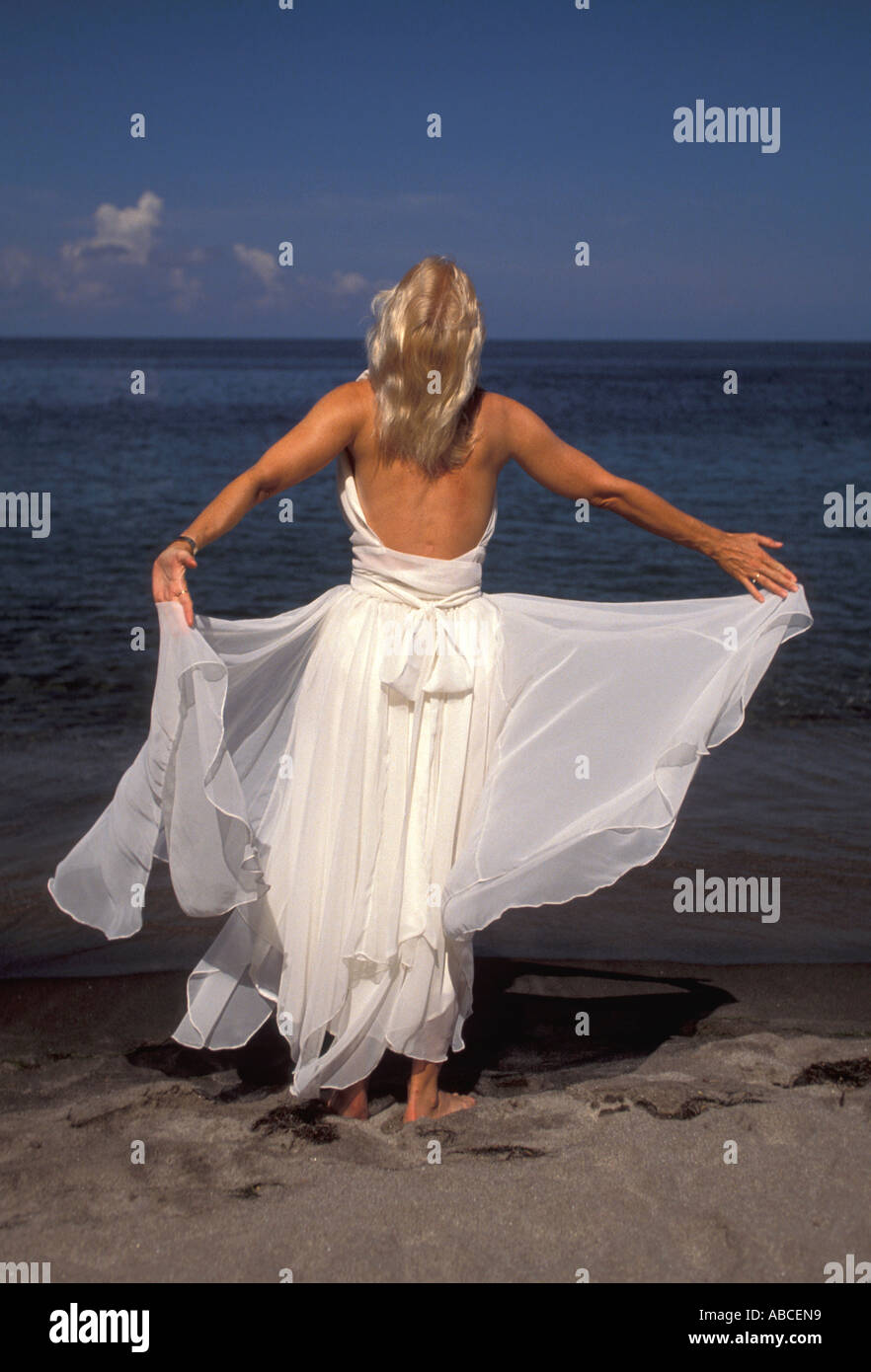 Caraïbes plage mariage femme seule avec écoulement blanc robe formelle est pieds nus sur le sable plage face à l'eau Banque D'Images