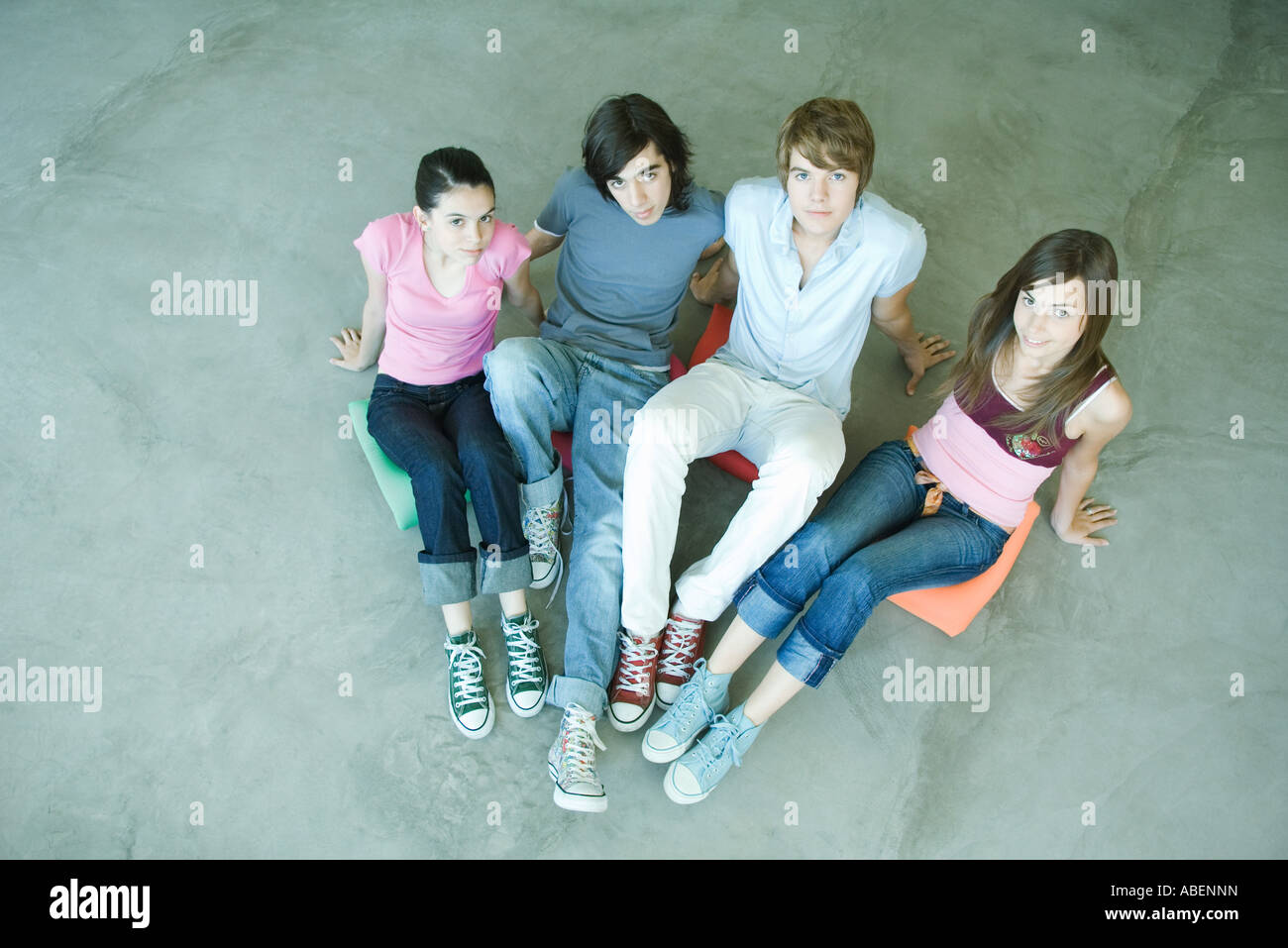 Quatre amis adolescents assis sur des coussins sur le sol, looking at camera, portrait Banque D'Images