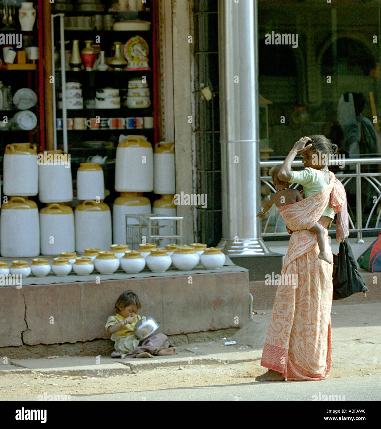 Une gitane se trouve sur le trottoir de la route alors que sa mère avec un bébé sur la hanche ressemble sur Kerala Inde du Sud Banque D'Images