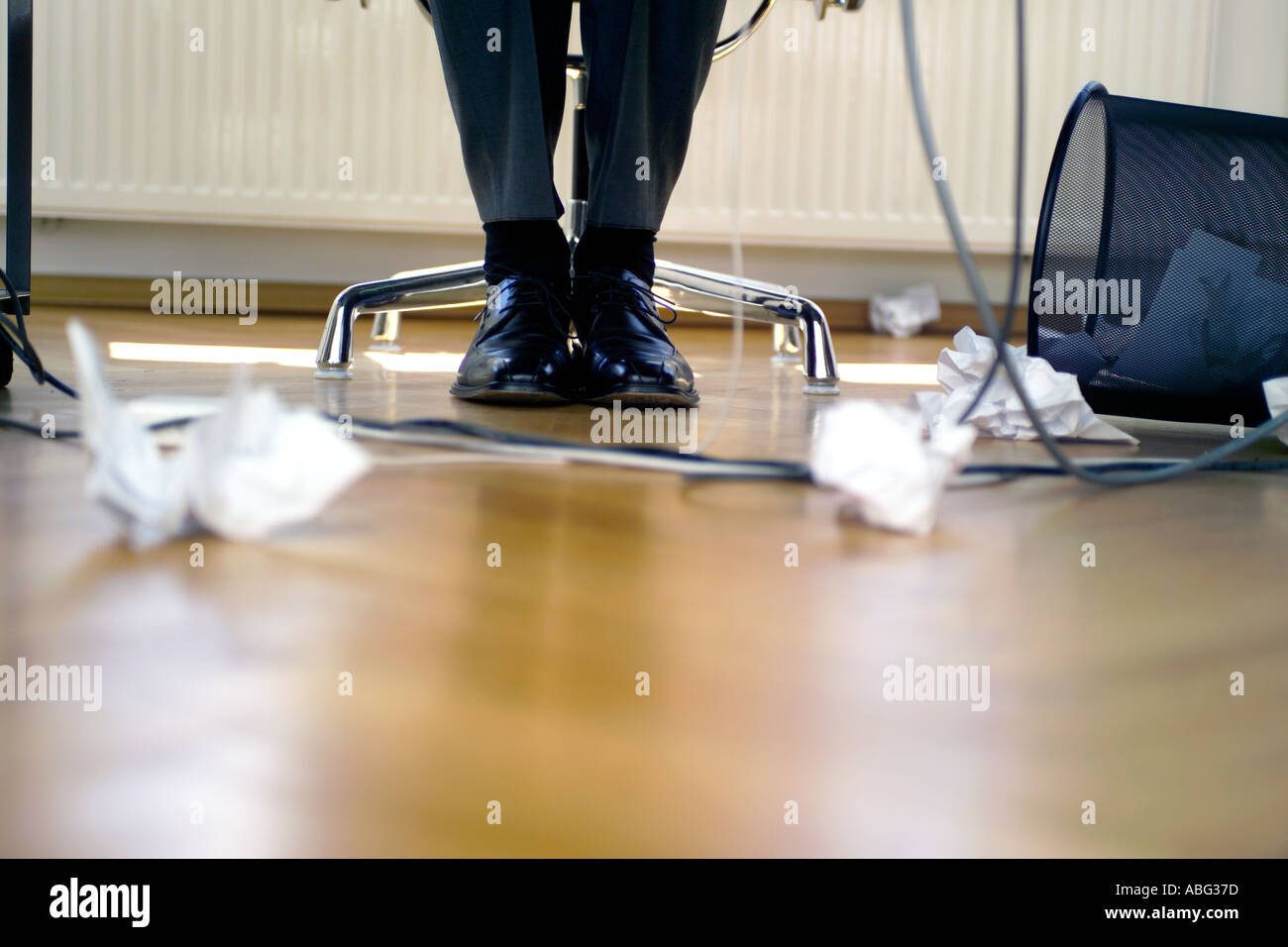 Les jambes de l'homme d'affaires sous la table Papier froissé et renversé poubelle se trouvant sur le plancher Banque D'Images