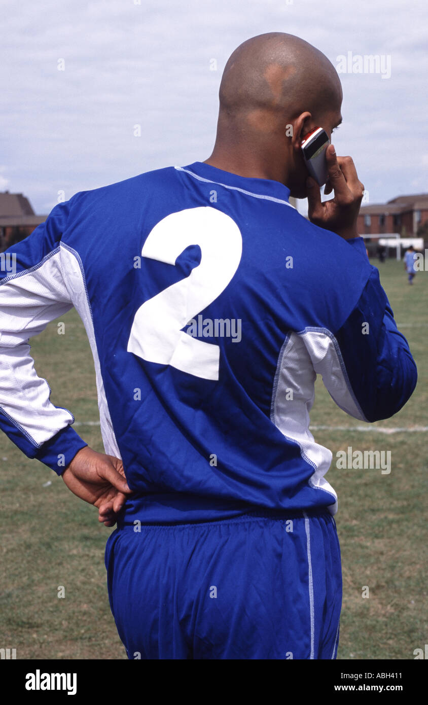 Footballeur amateur à l'aide d'un téléphone mobile pendant la mi-temps lors d'un jeu à Ipswich, Suffolk, UK. Banque D'Images