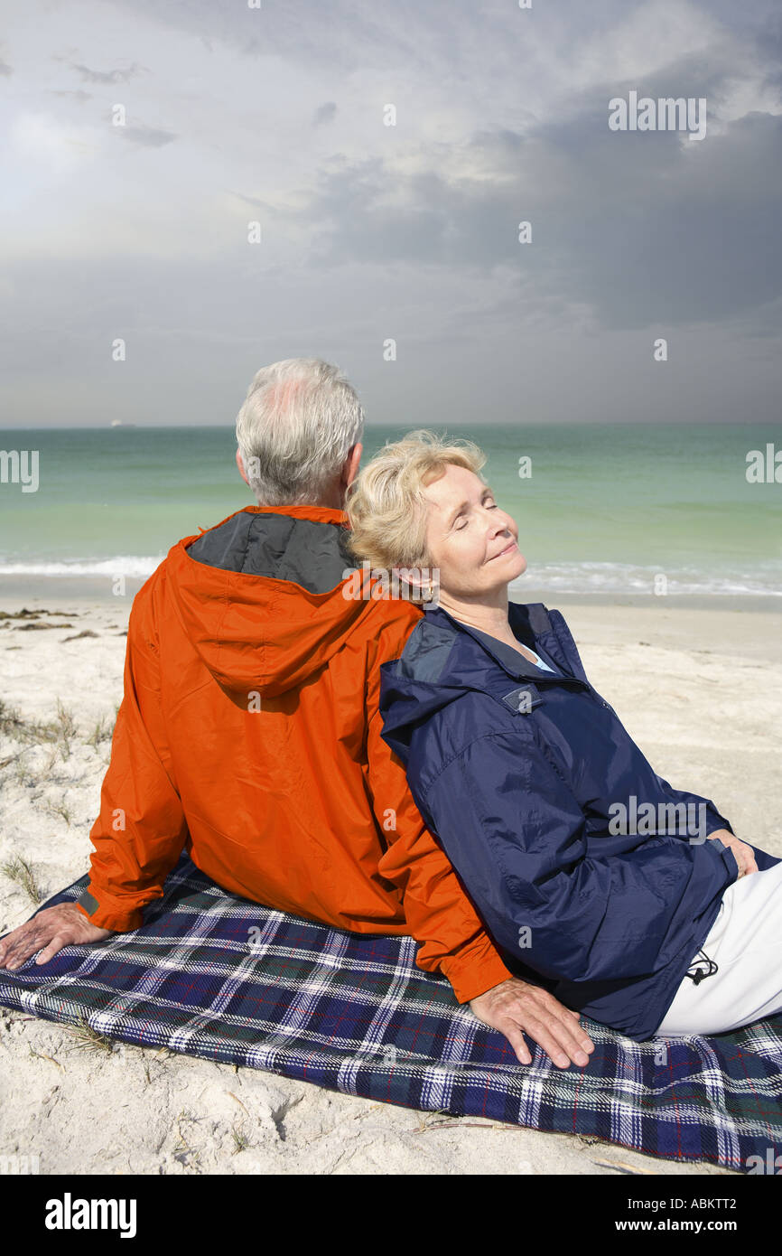 Photo de l'homme d'âge moyen et la femme assise sur la plage portant une couverture orange et bleu marine coupe-vent Banque D'Images