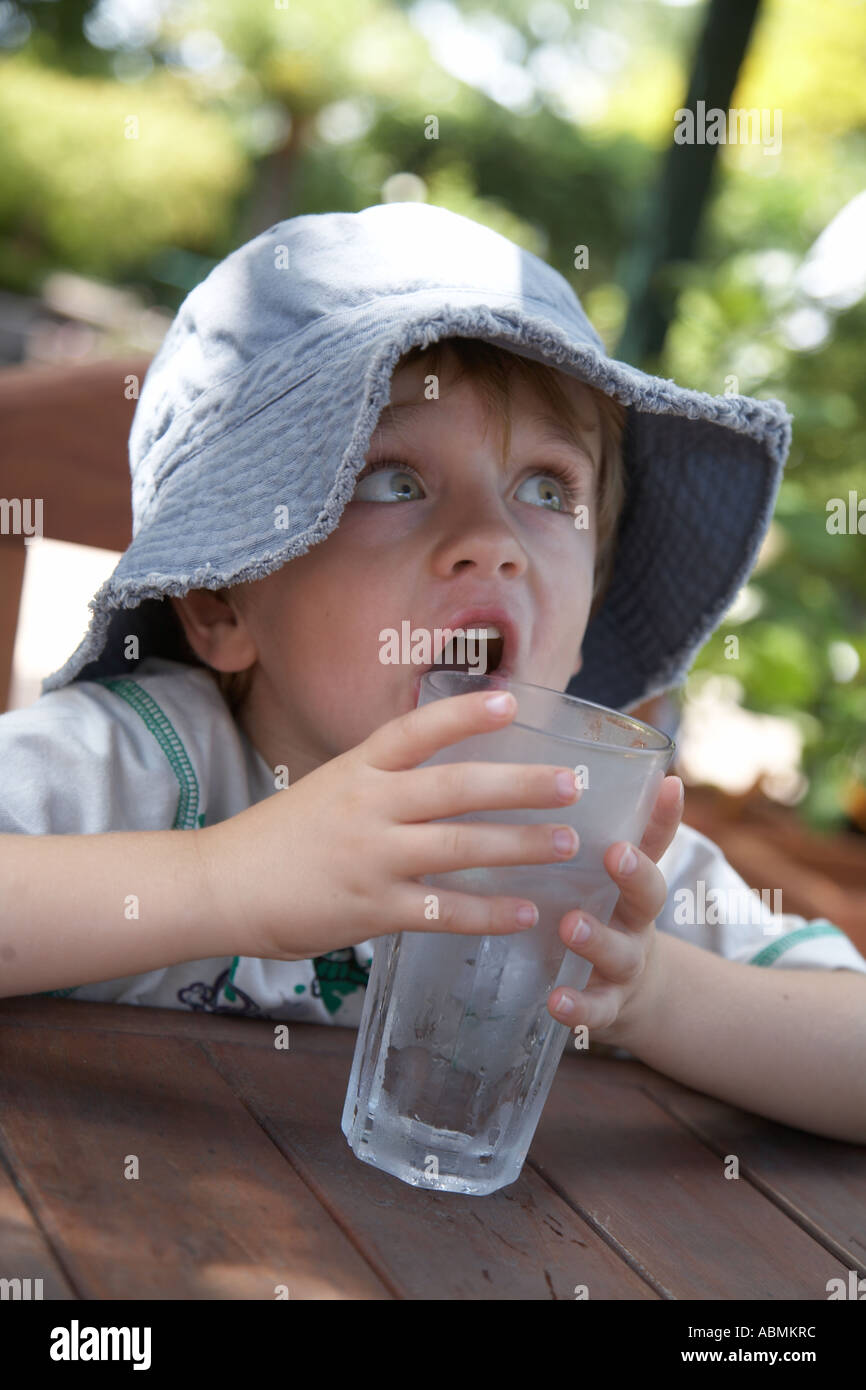 Jeune enfant en été le port floppy chapeau de soleil à la terrasse d'un café avec un grand verre d'eau fraîche Banque D'Images