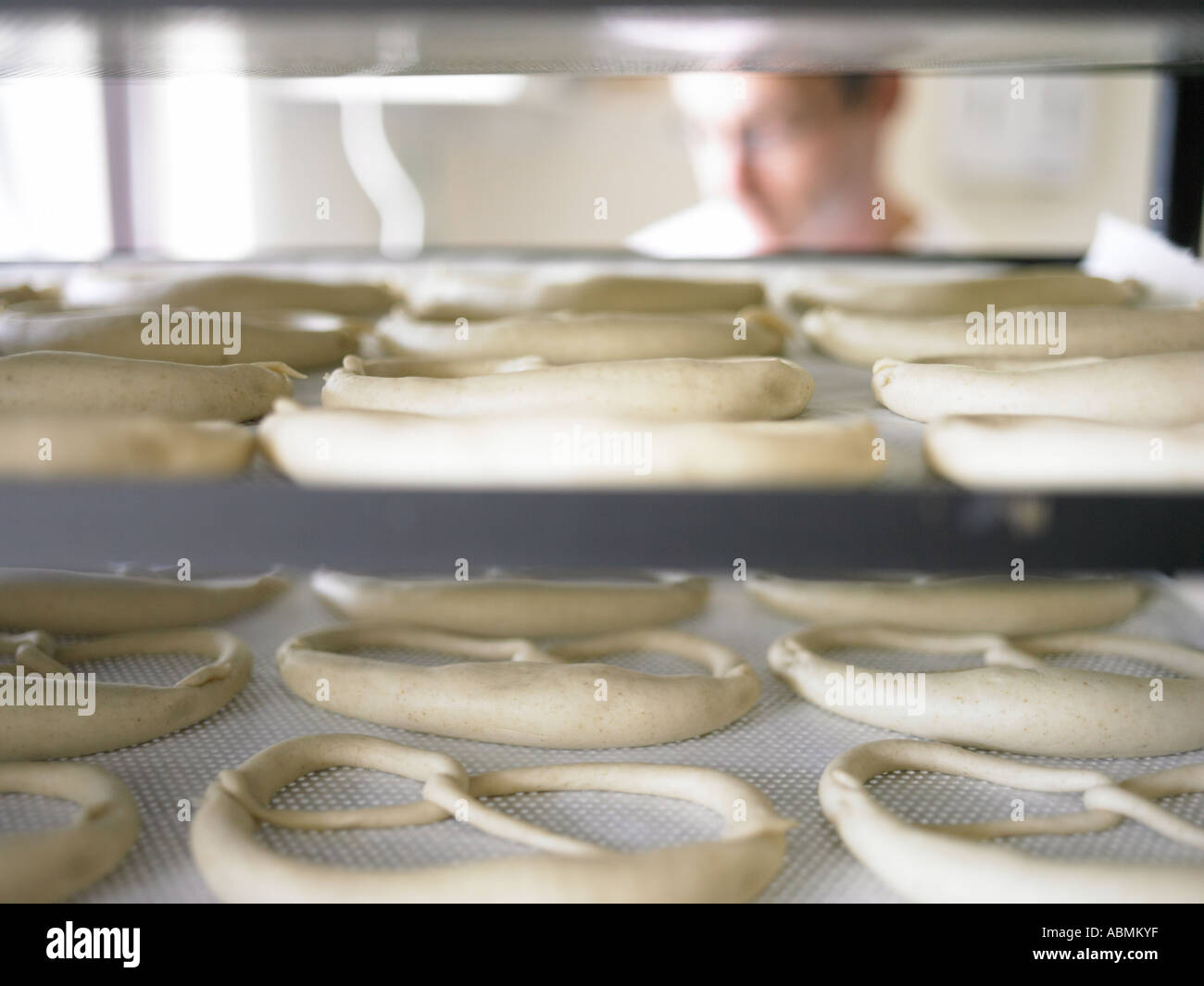 Dans la boulangerie baker mâle la cuisson du pain en petits brezels cuisine commerciale mis sur plaques de cuisson d'augmenter Banque D'Images