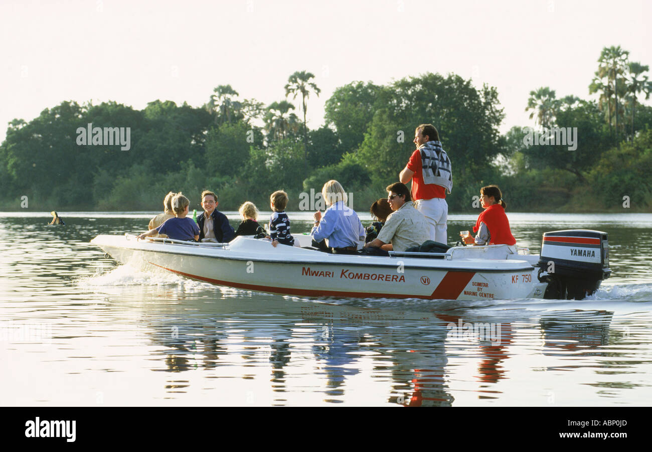 Les mâchoires s'étendant l'hippopotame dans le coucher du soleil au-delà de lumière rempli de touristes en bateau sur la rivière Zambèze Banque D'Images