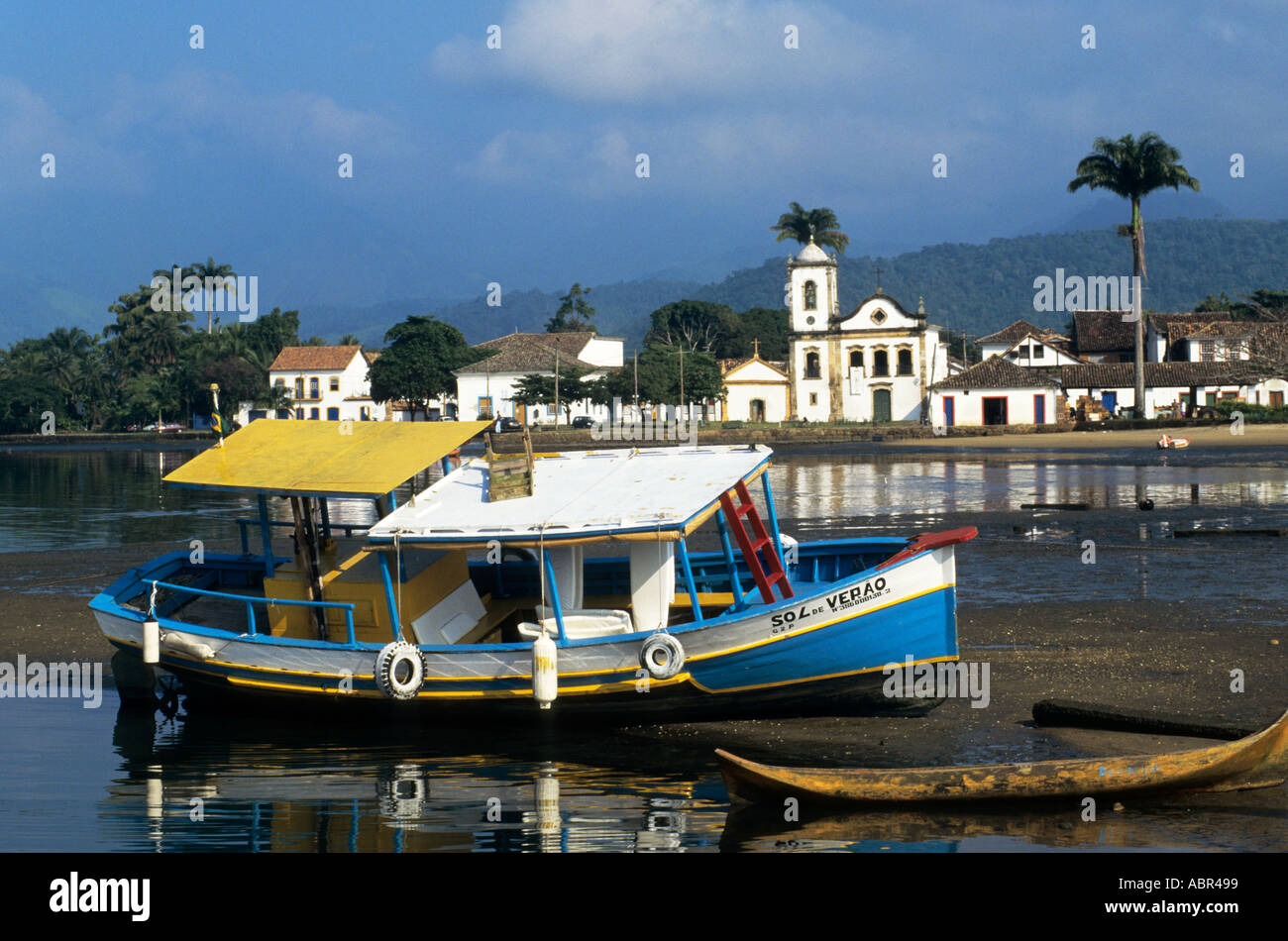 Paraty, Rio de Janeiro, Brésil ; État Sol de Verao bleu, jaune et blanc voile avec l'église coloniale de l'autre côté de la rivière. Banque D'Images