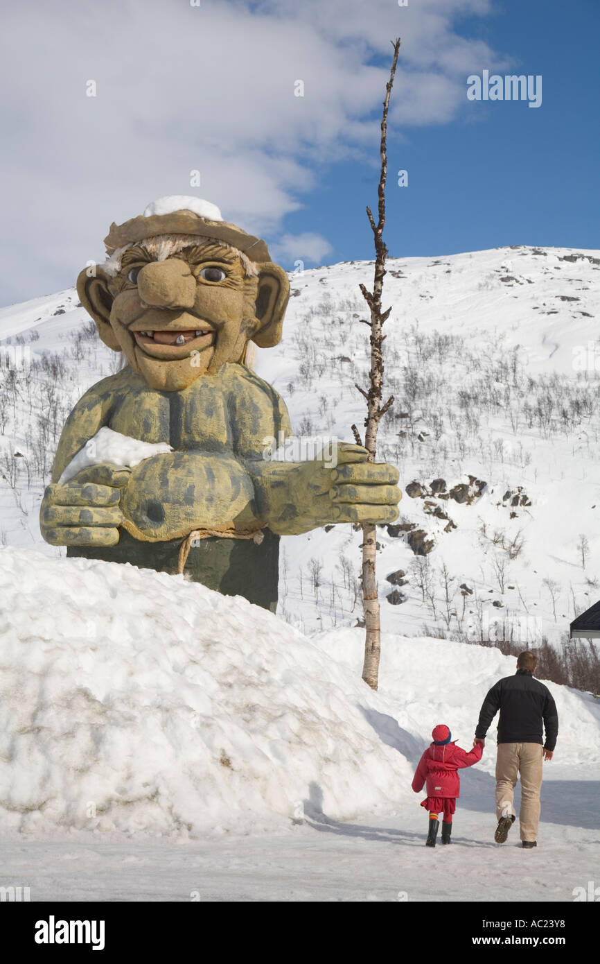 Un homme et une fille l'approche d'un énorme troll sculpture debout dans la neige en plus de la route européenne E 10 Banque D'Images