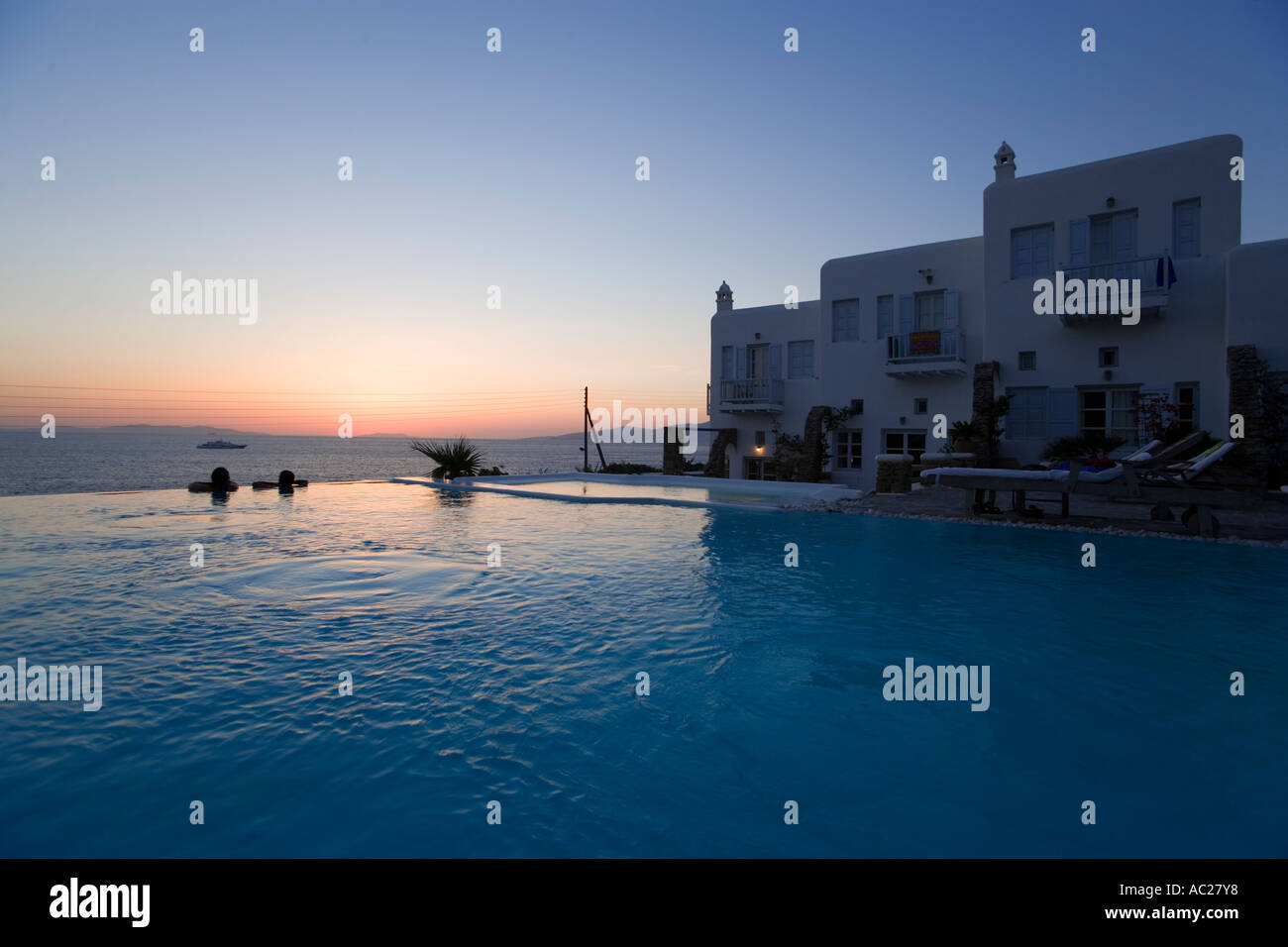 Les gens se trouvant dans la piscine d'eau douce et à la recherche sur la mer dans le crépuscule Apanema Resort Hotel Mykonos Grèce Banque D'Images