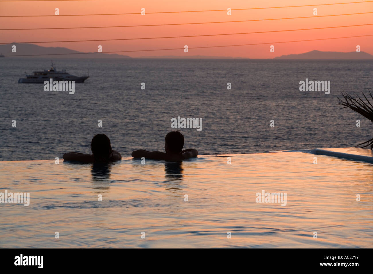 Les gens se trouvant dans la piscine d'eau douce et à la recherche sur la mer dans le crépuscule Apanema Resort Hotel Mykonos Grèce Banque D'Images